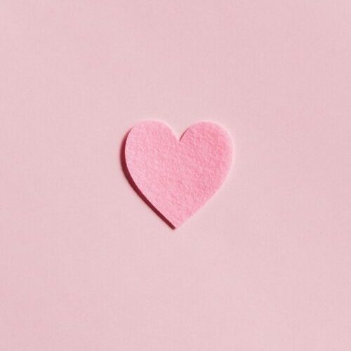 A simple pink felt heart on a light pink background, perfect for Valentine's Day themes.